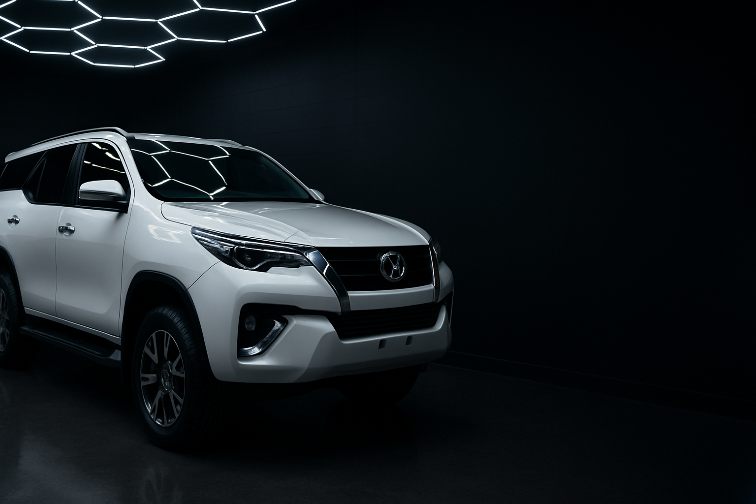 A gleaming white Toyota Fortuner parked in a dark detailing studio bay at night
